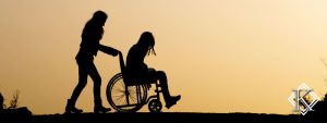 Silhueta de duas mulheres. Uma delas cadeirante e a outra empurrando a cadeira de rodas. Veja aqui informações a respeito da aposentadoria por invalidez.