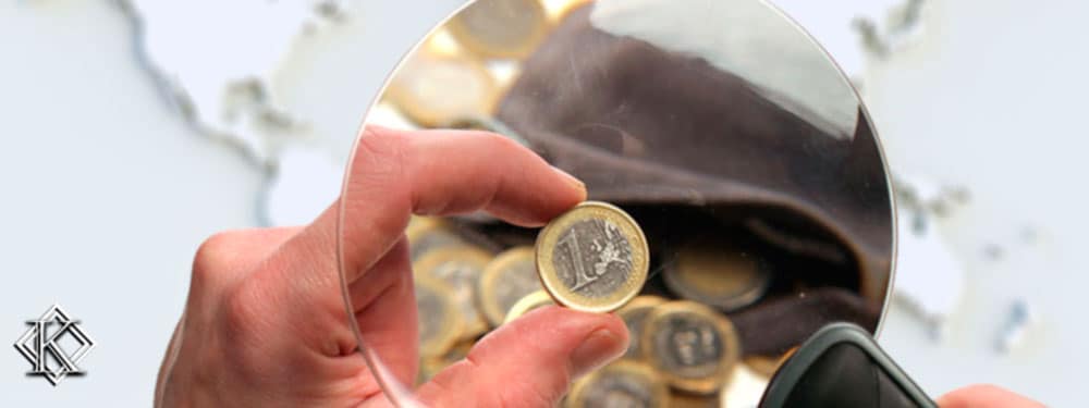 Um mão segurando uma lente de aumento verificando algumas moedas com um mapa de fundo, simbolizando as cobranças indevidas de aposentados no exterior