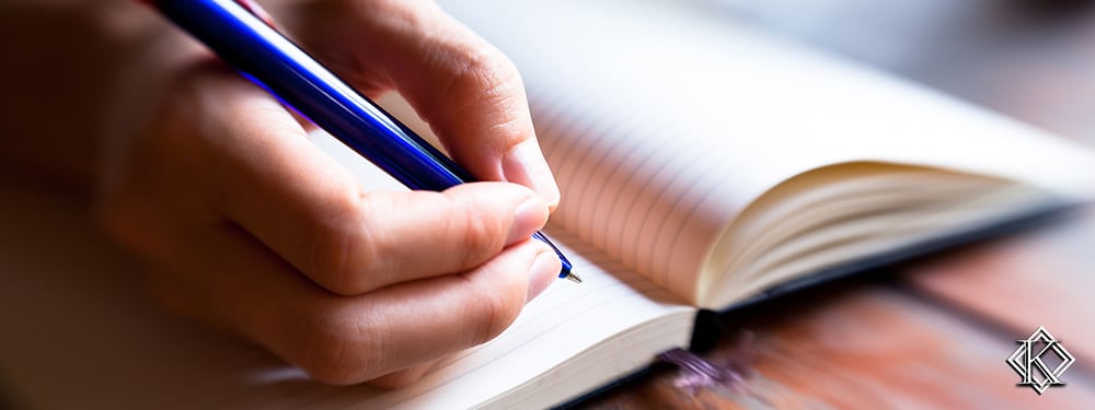 Uma mão anotando algo com uma caneta em um caderno. A imagem representa a atenção que é necessária ter em alguns fatores antes de entrar com o pedido de aposentadoria.