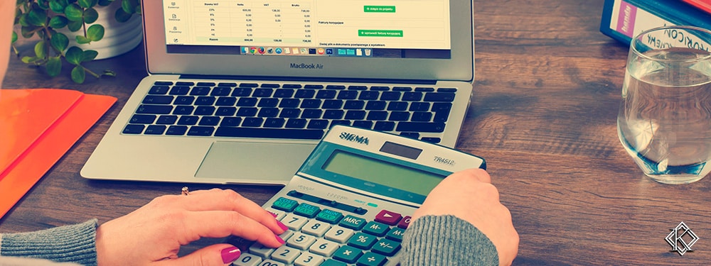 Uma mulher sentada a uma mesa com uma calculadora e um notebook montando uma planilha, representando a importância de fazer um planejamento financeiro e um planejamento de aposentadoria