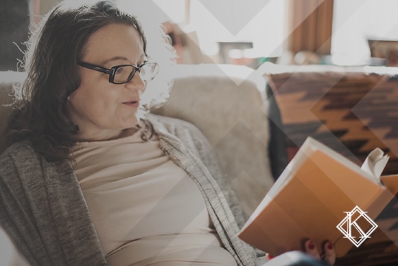 A imagem mostra uma mulher lendo um livro ou apostila no sofá, e ilustra a publicação 