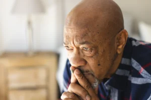 A imagem mostra um homem sênior negro, pensativo, com as mãos levadas a boca.