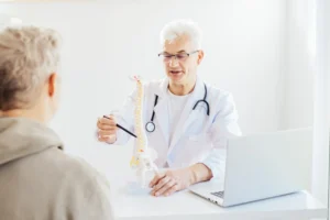 A imagem mostra um médico sênior, atendendo um paciente com problemas na coluna. Ilustra o texto se lombalgia aposenta.