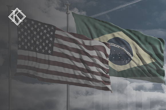 Imagem da bandeira dos Estados Unidos e Brasil, no fundo um céu azul com nuvens. A imagem tem um filtro cinza de acordo com a identidade visual da Koetz Advocacia. No canto superior esquerdo está a logo branca da Koetz Advocacia. A imagem ilustra o texto “Acordo previdência Estados Unidos e Brasil.”