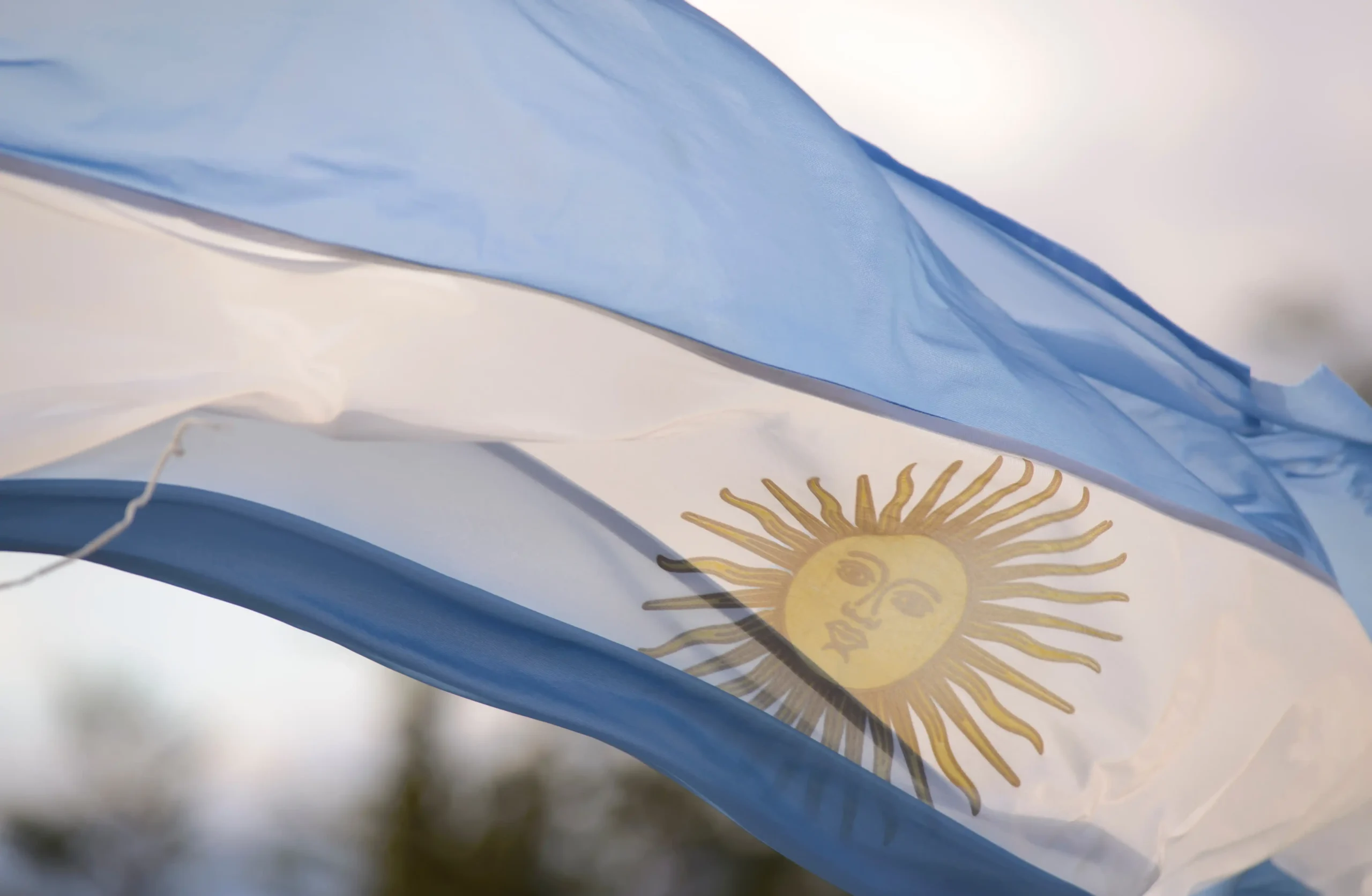 A imagem mostra a bandeira da Argentina, balançando ao vento. Ilustra o texto sobre Previdência da Argentina.