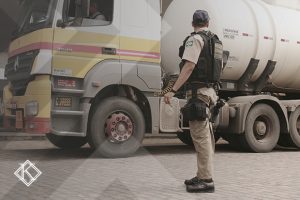A imagem mostra um policial federal rodoviário em frente a um caminhão. A imagem ilustra a publicação