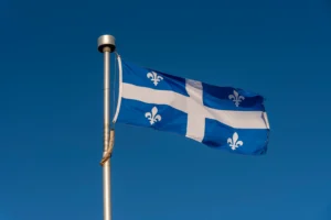 A imagem mostra a bandeira do Quebec, hasteada, balançando com o vento. Ilustra o texto sobre Acordo Previdenciário Quebec e Brasil.