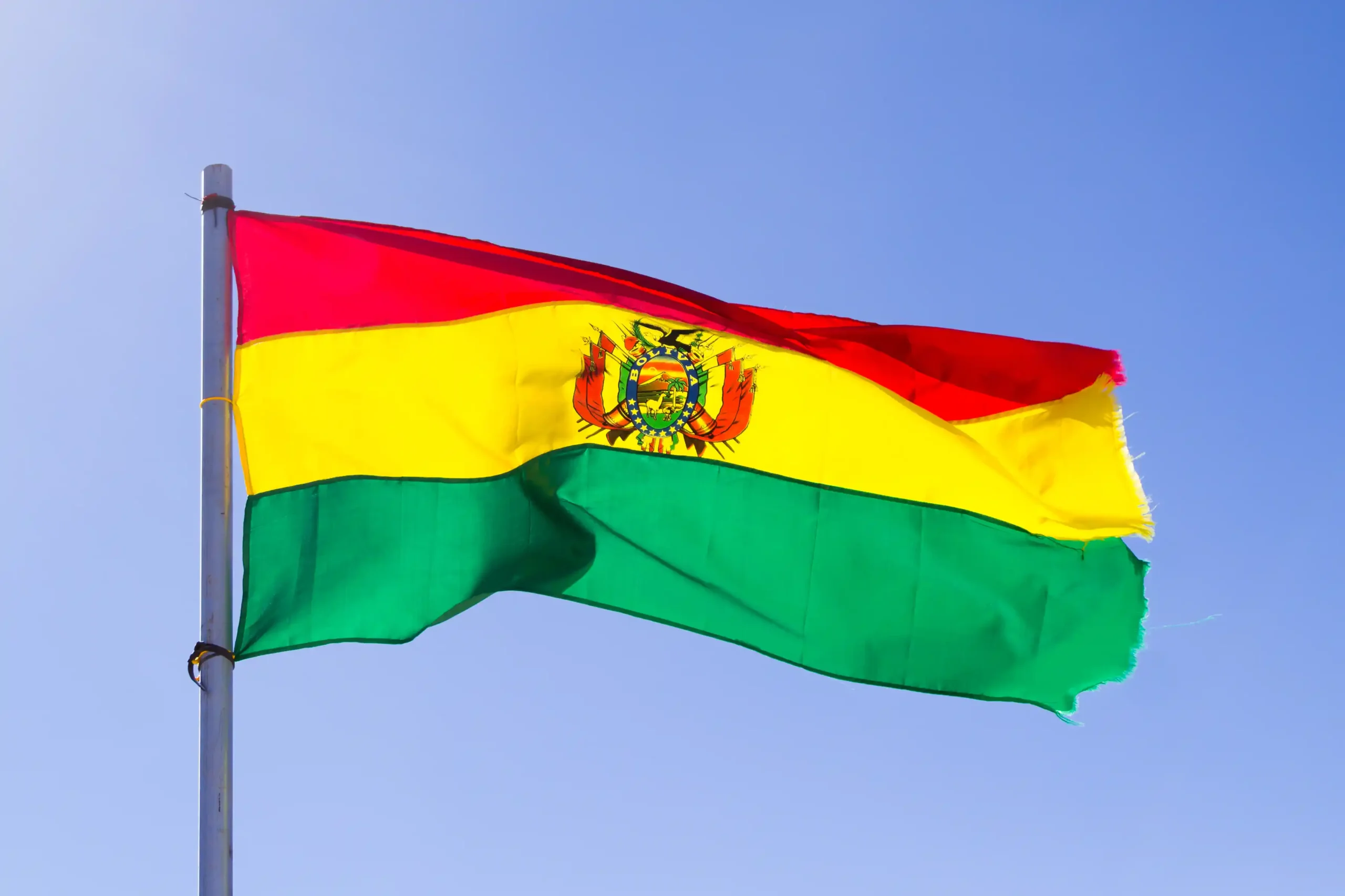 A imagem mostra a bandeira da Bolívia hasteada, balançando com o vento. Ilustra o texto sobre Acordo de Previdência entre Bolívia e Brasil.