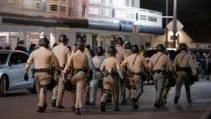 A imagem mostra um grupo de policiais andando pela rua.