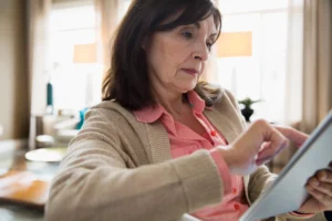 A imagem mostra uma mulher de meia-idade, utilizando um tablet.