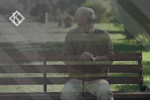 A imagem mostra um homem sentado em um banco de uma praça 