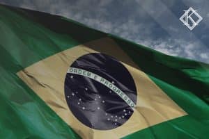 Close da bandeira do Brasil com céu azul no fundo. A imagem ilustra a publicação 