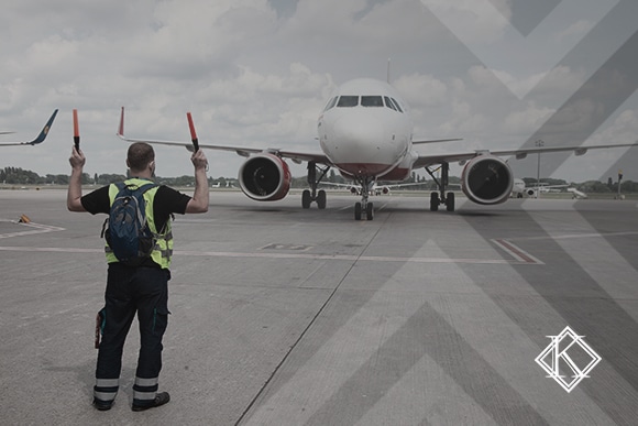 A imagem mostra um trabalhador aeroviário sinalizando para um avião, e ilustra a publicação 