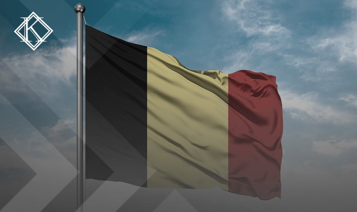 A imagem mostra uma bandeira da Bélgica, com o céu azul ao fundo. Ilustra a publicação 