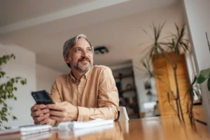 A imagem mostra um homem de meia-idade, sentado em uma cadeira, enquanto segura um smartphone. Ilustra o texto sobre direito adquirido na aposentadoria do servidor público.