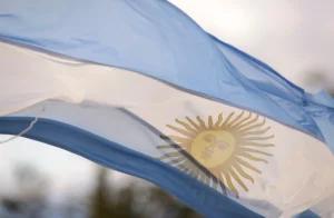 A imagem mostra a bandeira da Argentina hasteada, balançando com o vento. Ilustra o texto sobre como funciona a aposentadoria na Argentina.