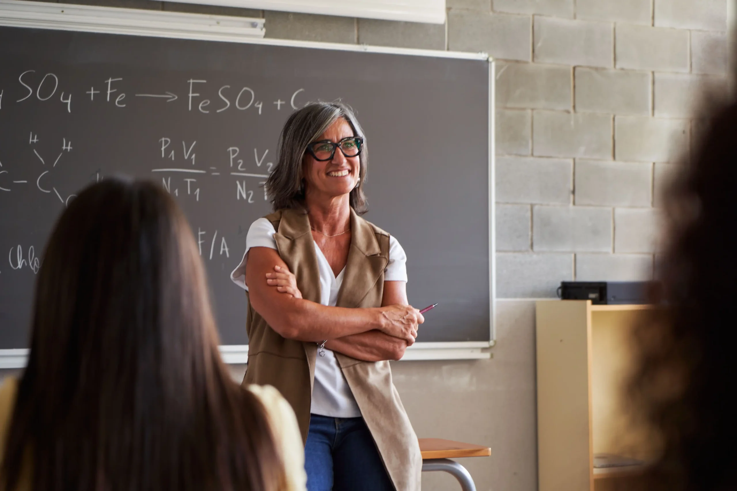 A imagem mostra uma professora de meia-idade, em frente à lousa, em sala de aula e ilustra o texto sobre Aposentadoria de professor universitário no INSS.