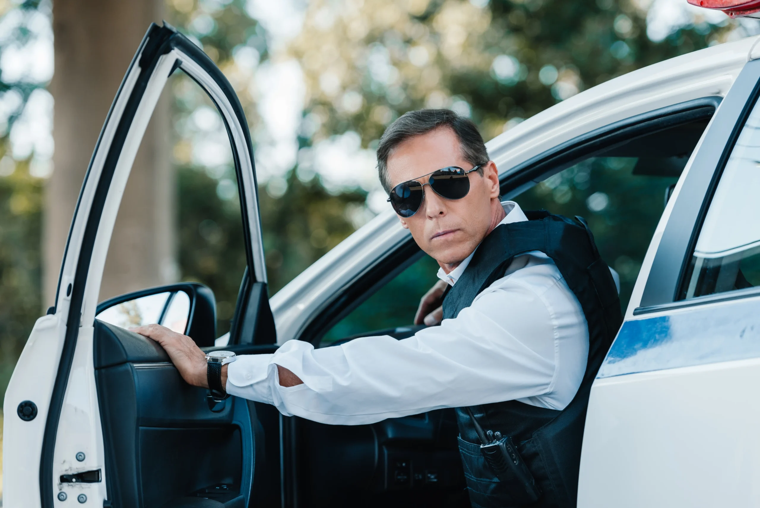 A imagem mostra um policial maduro em colete à prova de balas e óculos escuros saindo do carro. E ilustra o texto sobre periculosidade e aposentadoria especial.