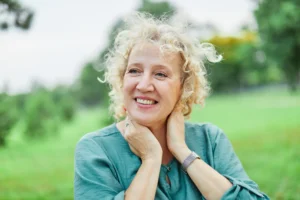 A imagem mostra uma mulher madura, sorrindo, ao ar livre. Ilustra o texto sobre idade mínima para aposentadoria por tempo.