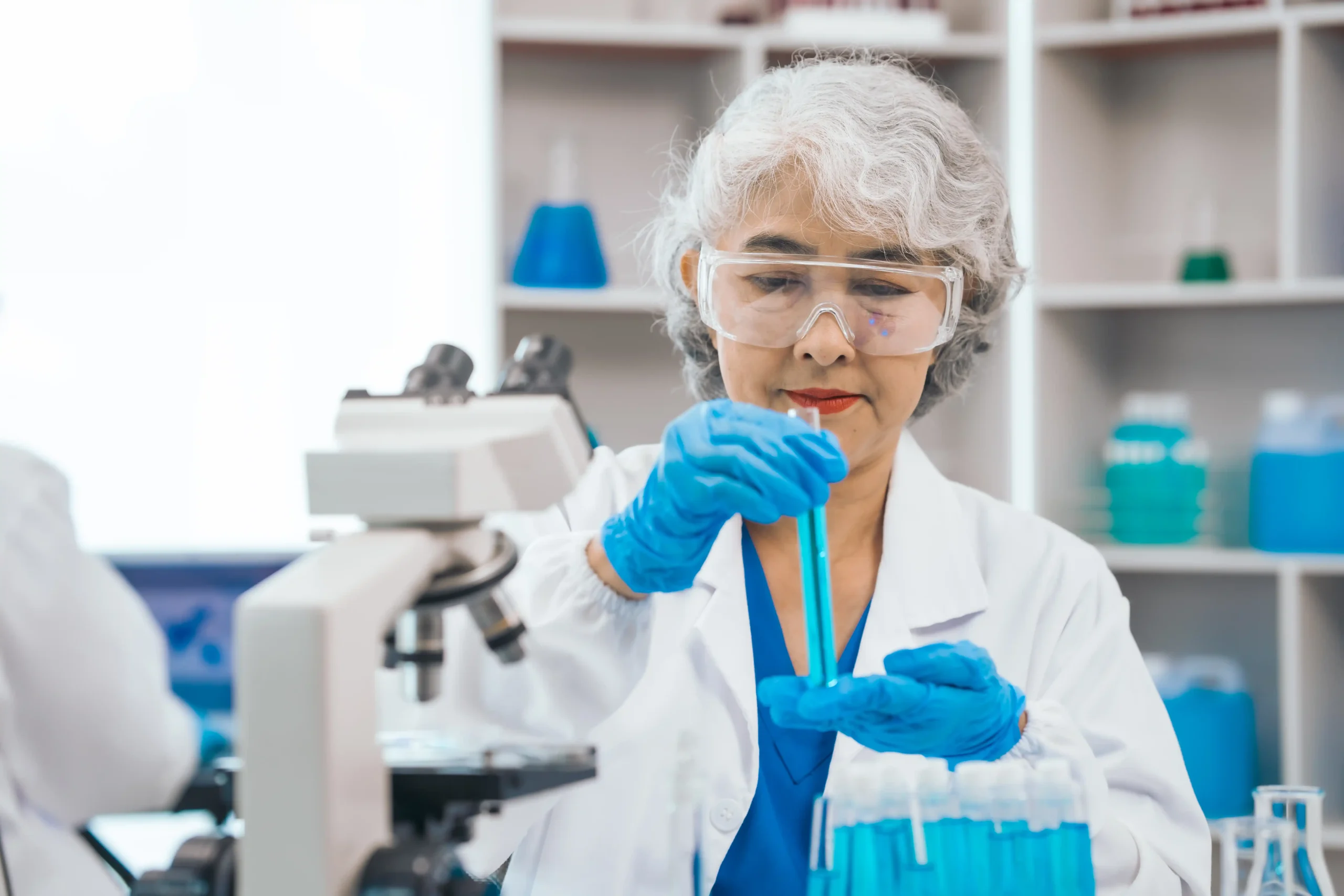 A imagem mostra uma mulher madura, com jaleco, trabalhando em laboratório. Ilustra o texto sobre aposentadoria especial do engenheiro químico.