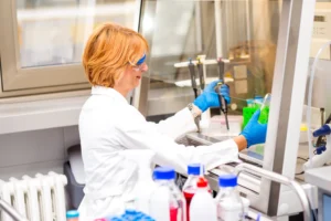 A imagem mostra uma mulher de meia-idade, de jaleco, trabalhando em um laboratório. Ilustra o texto sobre Periculosidade e insalubridade.