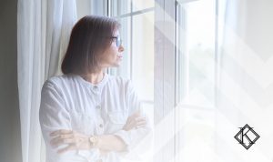 A imagem mostra uma mulher olhando pela janela, e ilustra a publicação aposentadoria de viúva, quais são as opções?, da Koetz Advocacia.