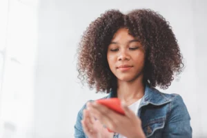 A imagem mostra uma adolescente segurando um smartphone com as mãos. Ilustra o texto sobre Pensão vai até que idade.