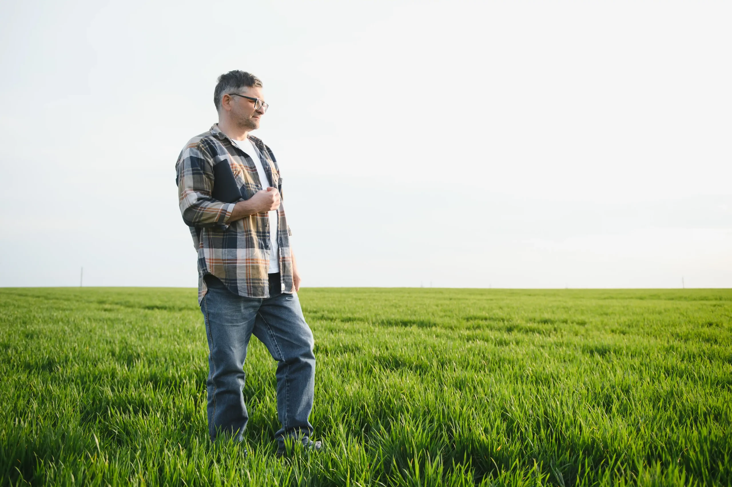 A imagem mostra um agricultor de meia idade, inspecionando o campo com um tablet na mão. Ilustra o texto sobre aposentadoria rural e documentos.