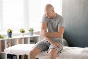 A imagem mostra um homem careca, tocando o cotovelo dolorido e tentando massageá-lo. Ilustra o texto sobre auxílio doença acidentário.