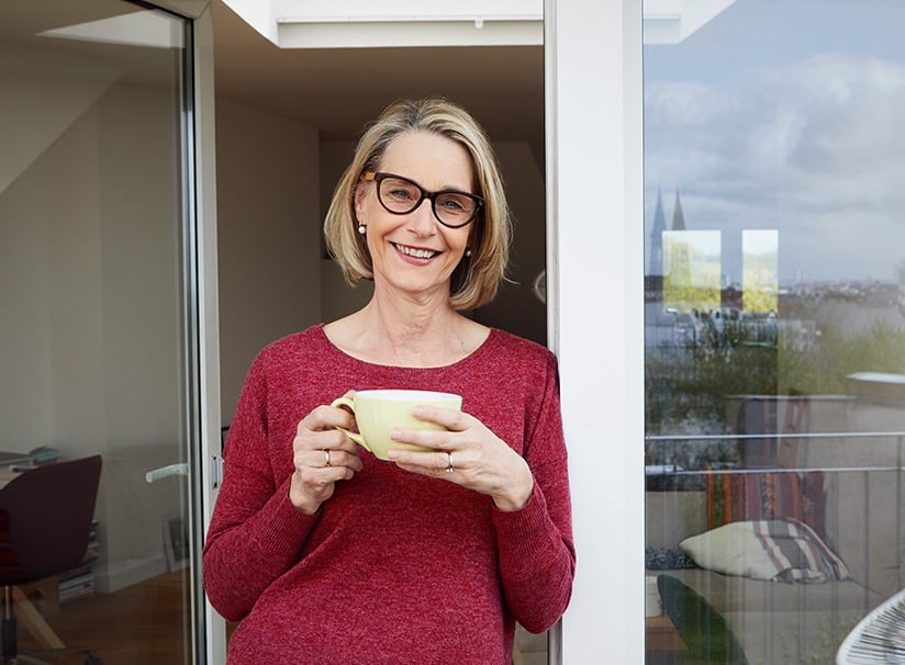 A imagem mostra uma mulher madura sorrindo para a camera tomando seu café. A imagem ilustra o texto 