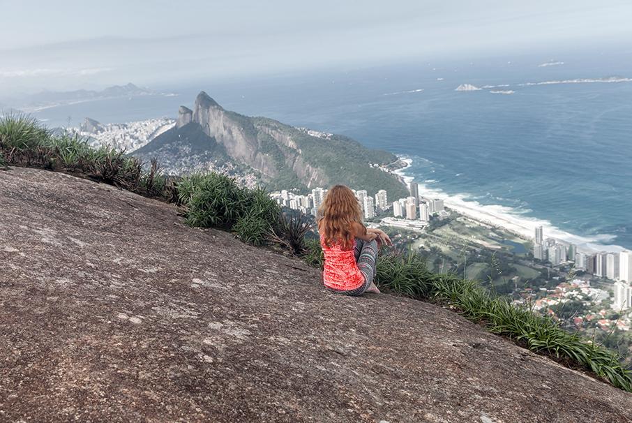 A imagem mostra uma mulher sentada em um pedra, de costas, observando a vista do Rio de Janeiro e ilustra o texto: Lugares para morar no Brasil: dicas para o estrangeiro escolher! da Koetz Advocacia.