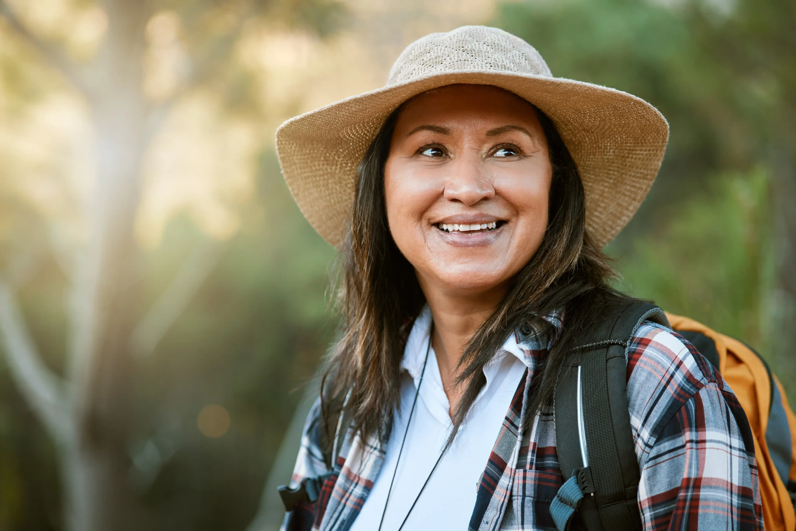 A imagem mostra uma mulher indígena sênior, fazendo uma caminhada ao ar livre. Ela usa um chapéu e está sorrindo. Ilustra o texto sobre aposentadoria indígena.