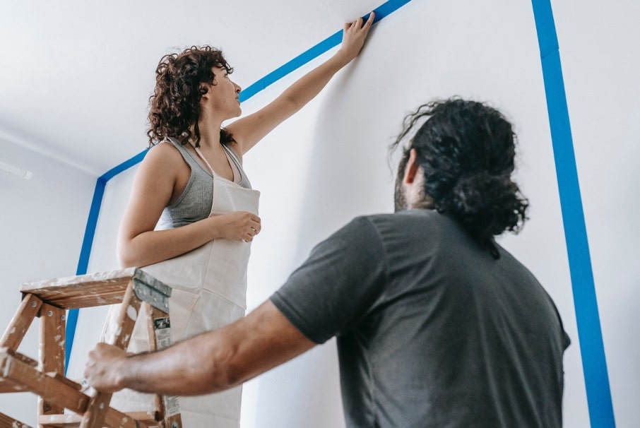 A imagem mostra um jovem casal reformando um cômodo da casa.