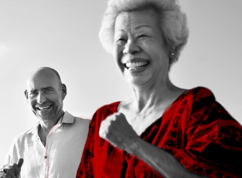 A imagem mostra um casal de idosos sorrindo, correndo ao ar livre.