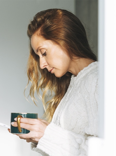 A imagem mostra uma mulher, de cabelos longos, com uma expressão séria, segurando uma xícara de café.