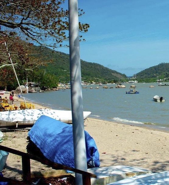 A imagem mostra uma praia em Florianópolis, onde barcos estão na areia.