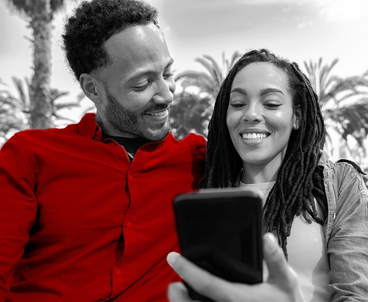 A imagem mostra um jovem casal negro, lado a lado, olhando para o celular, que está nas mãos da mulher.