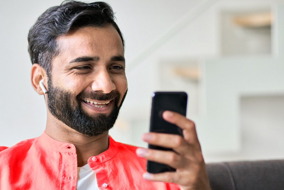 La imagen muestra a un hombre sonriente usando su teléfono celular, ilustrando el articulo "residencia permanente para extranjeros en Brasil"