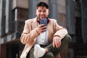 La imagen muestra a un joven latino sonriendo con su celular. ilustrando el articulo 