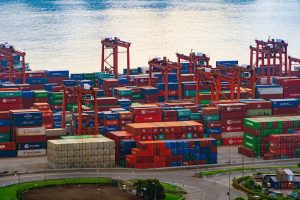 A imagem mostra vários containers em navios, a beira mar e ilustra o texto: Incoterms and International Transportation of goods da Koetz Advocacia.