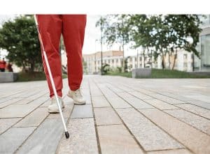 A imagem mostra um homem cego, segurando um bastão enquanto anda pela cidade. A imagem ilustra o texto 