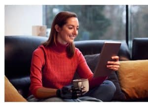 A imagem mostra uma mulher com braço protético, usando um tablet e segurando uma xicara de café. A imagem ilustra o texto 