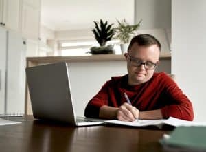 A imagem mostra um homem com síndrome de down, aprendendo algo, com seu notebook ao lado. A imagem ilustra o texto 