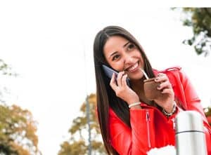 A imagem mostra uma mulher jovem, falando ao telefone enquanto bebe mate. A imagem ilustra o texto 