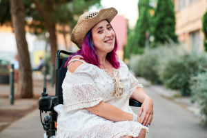 A imagem mostra uma jovem mulher com deficiência, em uma cadeira de rodas, sorrindo para a câmera e ilustra o texto: Direitos da pessoa com deficiência no INSS da Koetz Advocacia.