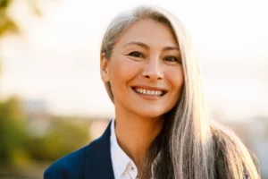 A imagem mostra uma mulher madura, de cabelos longos grisalhos. Ela está sorrindo, olhando diretamente para a câmera. E ilustra o texto sobre aposentadoria para autônomo.