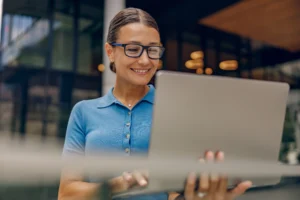 A imagem mostra uma mulher sorridente, utilizando um laptop. Ilustra o texto sobre alíquotas do INSS.