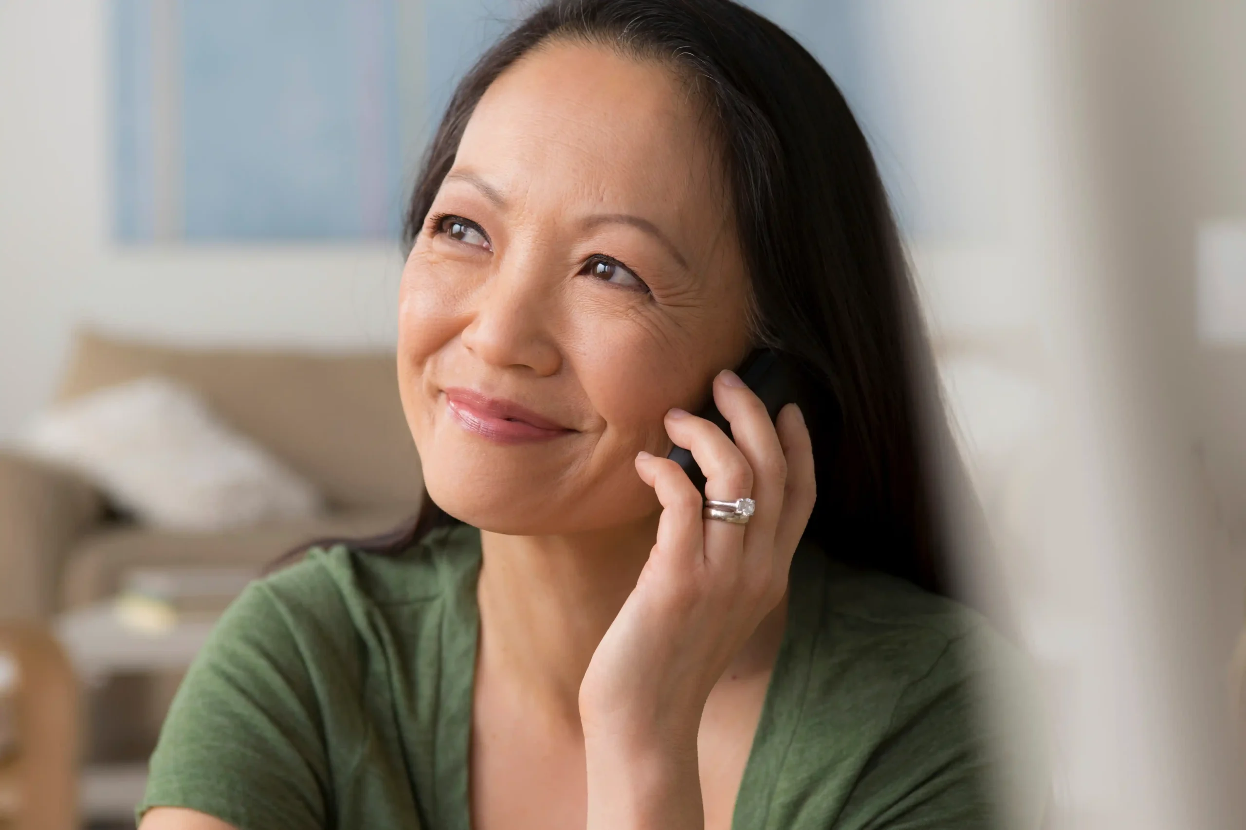 A imagem mostra uma mulher de meia-idade, sorrindo, enquanto utiliza um smartphone.