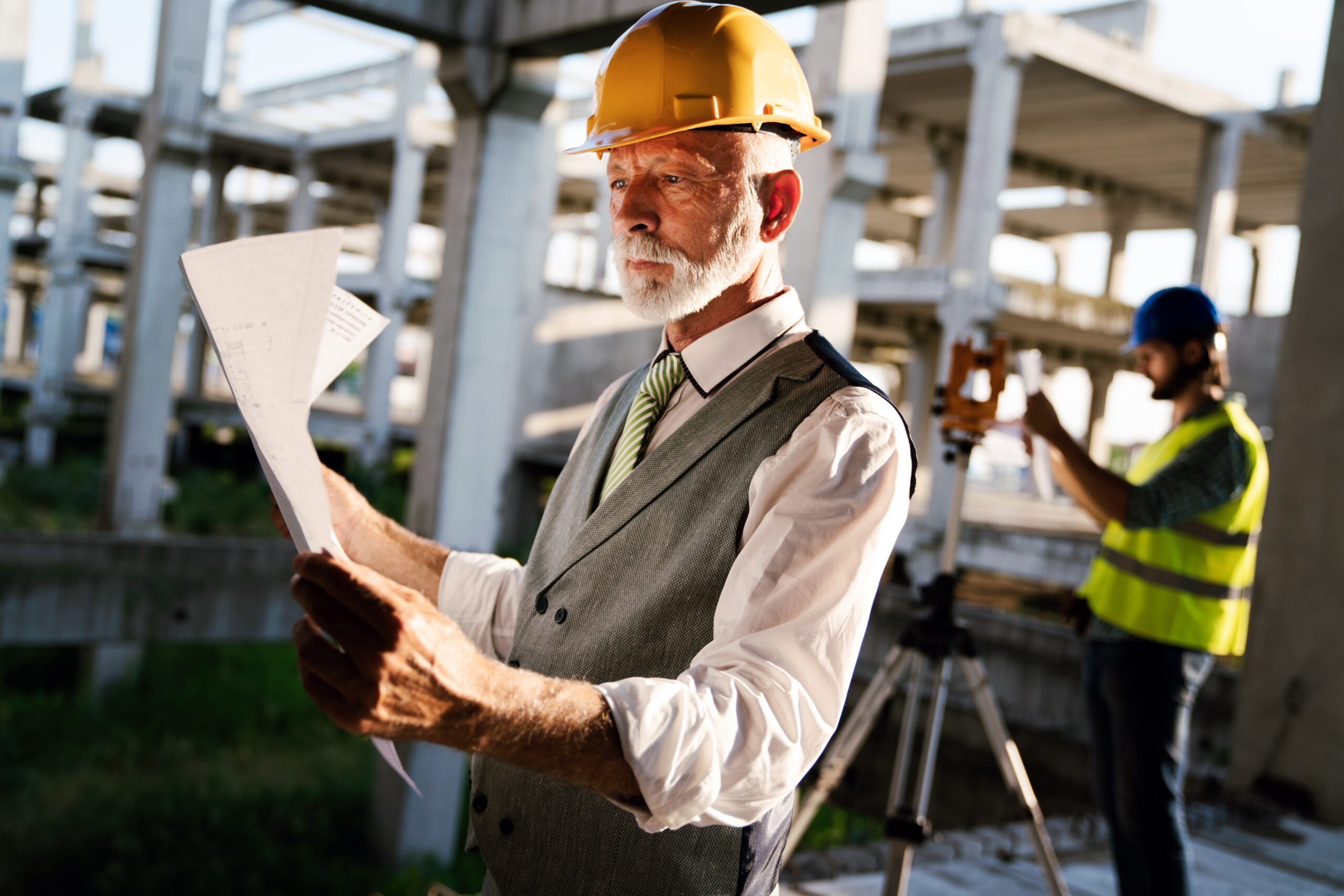 A imagem mostra um engenheiro civil sênior, segurando um projeto com as mãos, utilizando um capacete em meio a uma obra. Ilustra o texto sobre Aposentadoria Especial do Engenheiro Civil.