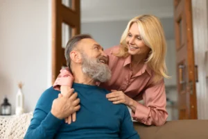 A imagem mostra um casal de meia-idade, em casa, sorrindo um para outro. Ilustra o texto sobre aposentadoria do brasileiro no exterior.